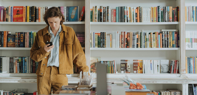 A young man looks at a smartphone in a library.