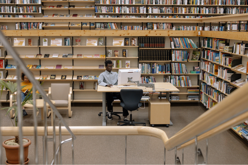 man sits in front of a computer in a library