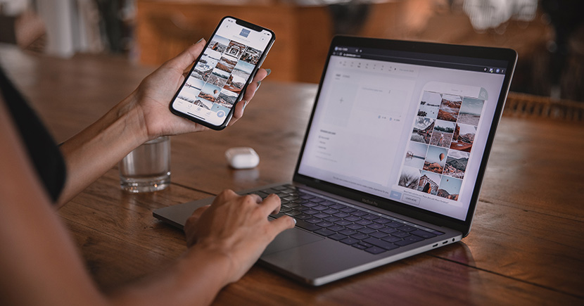 female hand holding a phone in her left hand and using a laptop with her right hand